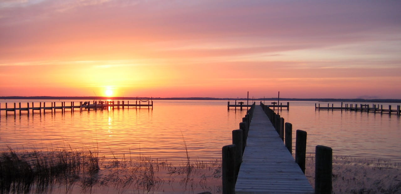 Sunset illuminates the sky with docks leading to a body of water in the foreground