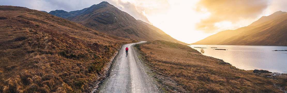 Person biking along a winding road at sunrise, symbolizing a mid-year financial check-in and progress toward long-term goals.