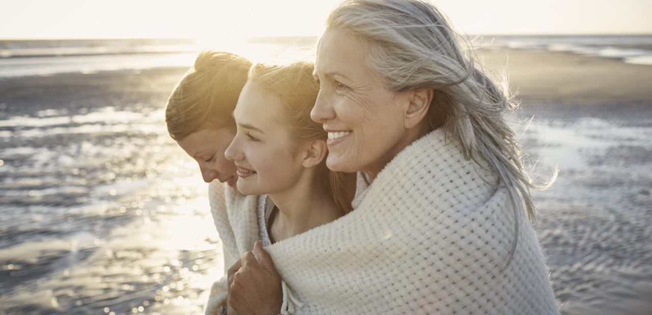 Grandmother, mother and daughter wrapped in a blanket on the beach