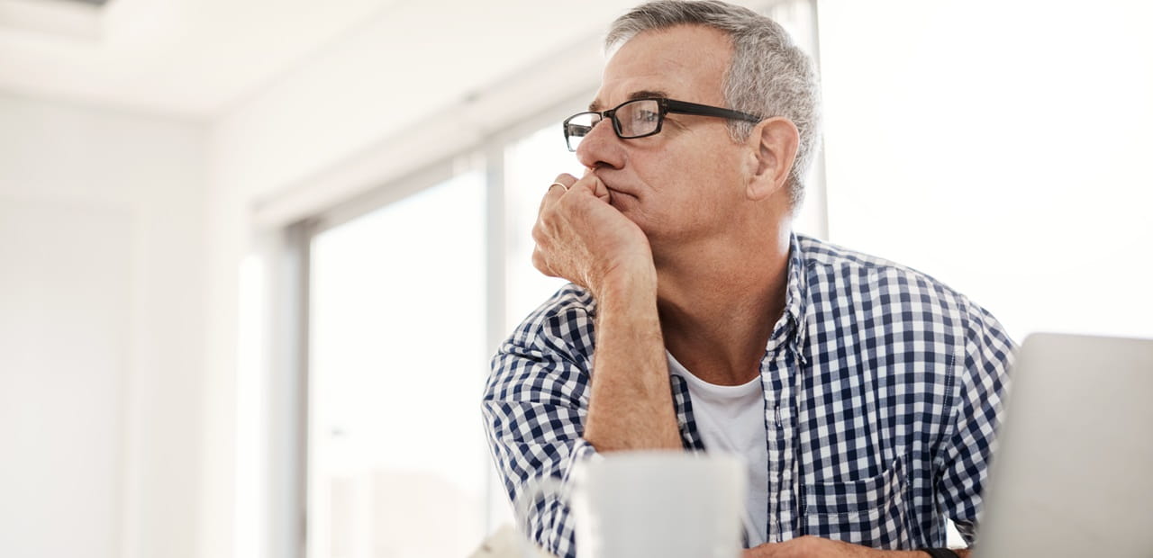 hot of a mature man looking thoughtful while working on a laptop at home